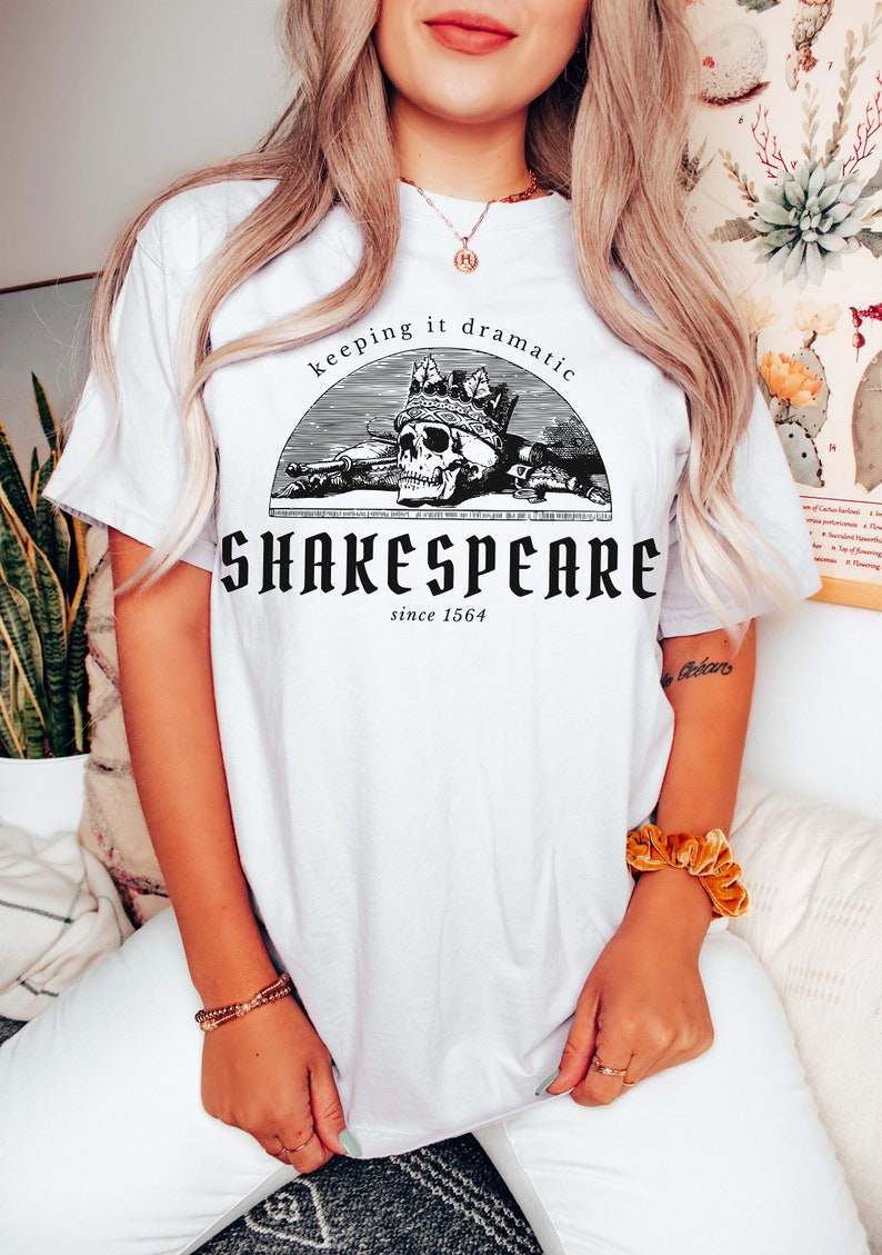 May include: White t-shirt featuring a black and white graphic of a skull wearing a crown. The graphic is in a circle with the text "keeping it dramatic" above the skull and "SHAKESPEARE since 1564" below the skull.