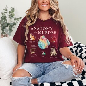 May include: A maroon t-shirt with the text "Anatomy of a Murder" and illustrations of a cat, a tie-dye hoodie, a ring, a metal object, a green gem, and a dog.