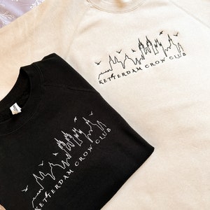 May include: Two sweatshirts, one black and one beige, with a skyline graphic and the text "Ketterdam Crow Club".