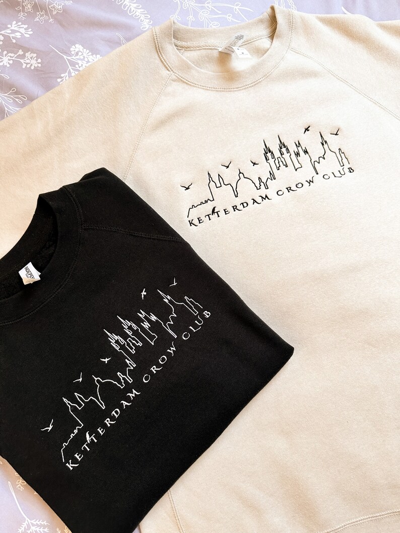 May include: Two sweatshirts, one black and one beige, with a skyline graphic and the text "Ketterdam Crow Club".