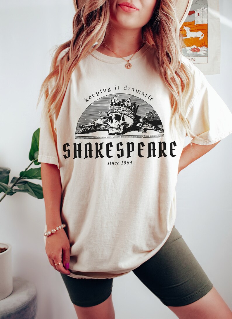 May include: A cream-coloured t-shirt with a black graphic of a skull wearing a crown and the text "keeping it dramatic" above the skull and "SHAKESPEARE since 1564" below the skull.