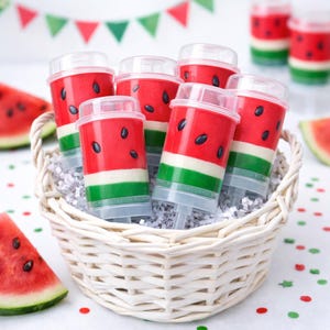 May include: A white wicker basket filled with watermelon-themed push-pop treats. The push-pops feature a red exterior with black seed details, green and white stripes, and clear lids. Slices of watermelon are also visible.
