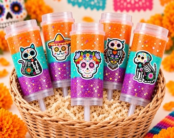 May include: Five clear plastic push-pop containers filled with layered orange, teal, and purple glittery gel. Each container features a different sticker: a cat, a skull with a sombrero, a floral skull, an owl, and a dog, all in a skeleton style.