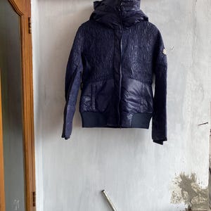 Puede incluir: Chaqueta acolchada azul marino con capucha. La chaqueta tiene un patrón texturizado en la parte superior y una sección inferior lisa y acolchada. Cuenta con cierre de cremallera y dobladillo y puños acanalados.