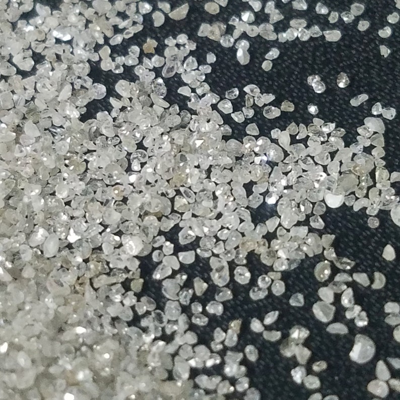 Puede incluir: Primer plano de una dispersi&oacute;n de peque&ntilde;as piedras preciosas claras y brillantes. Las piedras preciosas tienen forma irregular y reflejan la luz, creando un efecto brillante. El fondo es una superficie oscura y texturizada.