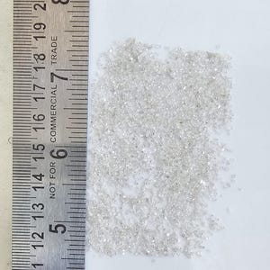 Puede incluir: Un mont&oacute;n de peque&ntilde;os diamantes transparentes junto a una regla met&aacute;lica. La regla muestra medidas en cent&iacute;metros, con los n&uacute;meros 28 a 50. Los diamantes est&aacute;n dispersos sobre una superficie blanca.