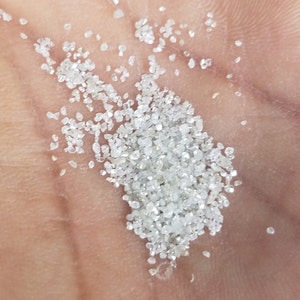 Puede incluir: Primer plano de un pu&ntilde;ado de peque&ntilde;os cristales de diamante claros y brillantes. Los cristales, de tama&ntilde;os y formas variadas, est&aacute;n dispersos sobre una superficie de color piel, reflejando la luz.
