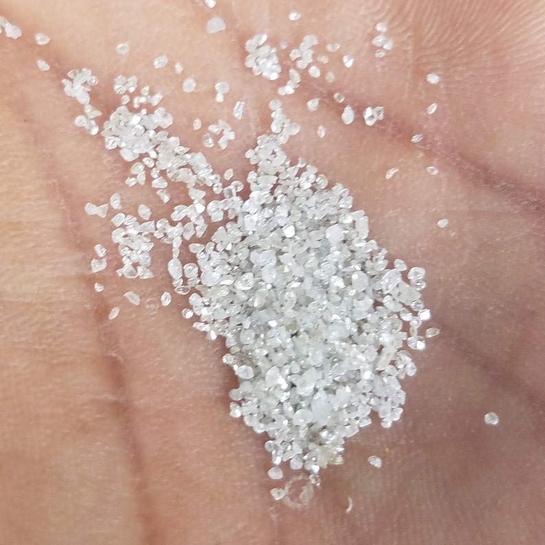 Puede incluir: Primer plano de un pu&ntilde;ado de peque&ntilde;os cristales de diamante claros y brillantes. Los cristales, de tama&ntilde;os y formas variadas, est&aacute;n dispersos sobre una superficie de color piel, reflejando la luz.