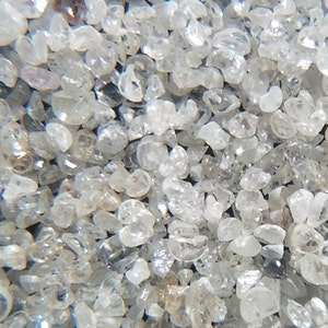 Puede incluir: Primer plano de un mont&oacute;n de peque&ntilde;os cristales de cuarzo claros y transl&uacute;cidos. Los cristales tienen forma irregular y var&iacute;an en tama&ntilde;o, con una calidad brillante y reflectante. El color general es una mezcla de claro y gris claro.