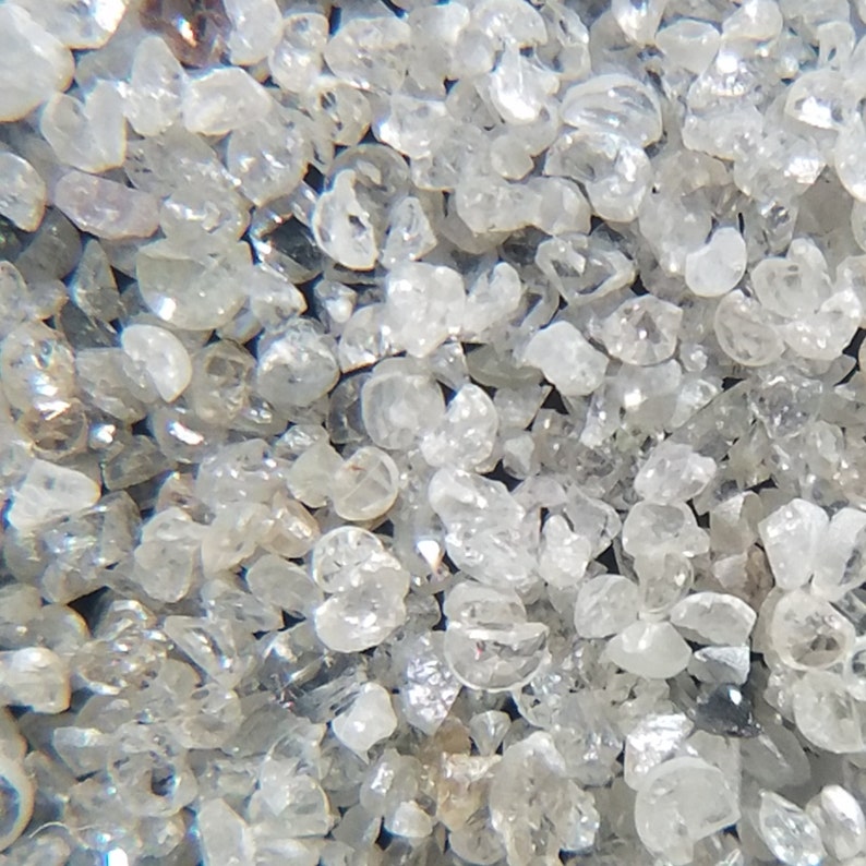 Puede incluir: Primer plano de un mont&oacute;n de peque&ntilde;os cristales de cuarzo claros y transl&uacute;cidos. Los cristales tienen forma irregular y var&iacute;an en tama&ntilde;o, con una calidad brillante y reflectante. El color general es una mezcla de claro y gris claro.