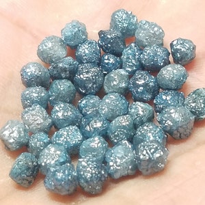 May include: A collection of blue rough diamonds, also known as raw diamonds, with a silvery sheen. These diamonds are unpolished and have a natural, irregular shape.