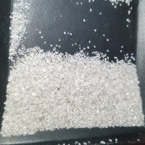 Puede incluir: Una colecci&oacute;n de peque&ntilde;as gemas claras y facetadas, posiblemente diamantes o cristales similares, se dispersan sobre una superficie oscura. Las gemas var&iacute;an en tama&ntilde;o y forma, con una calidad brillante y reflectante. El efecto general es de brillo y lujo.