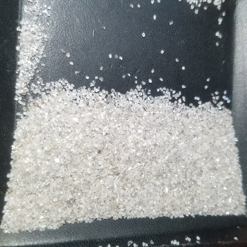 Puede incluir: Una colecci&oacute;n de peque&ntilde;as gemas claras y facetadas, posiblemente diamantes o cristales similares, se dispersan sobre una superficie oscura. Las gemas var&iacute;an en tama&ntilde;o y forma, con una calidad brillante y reflectante. El efecto general es de brillo y lujo.