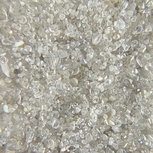 Puede incluir: Primer plano de una colecci&oacute;n de peque&ntilde;os cristales claros e irregulares. Los cristales est&aacute;n densamente empaquetados, creando una superficie texturizada y brillante. La luz se refleja en las facetas, dando una apariencia brillante y reluciente. El color general es blanco transl&uacute;cido.