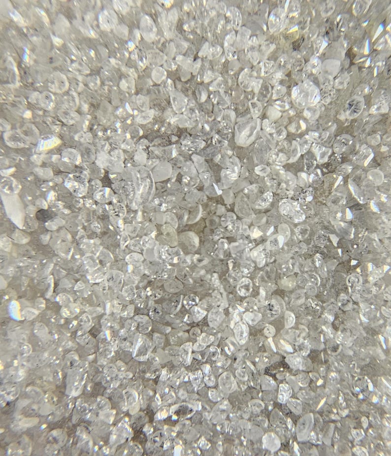 Puede incluir: Primer plano de una colecci&oacute;n de peque&ntilde;os cristales claros e irregulares. Los cristales est&aacute;n densamente empaquetados, creando una superficie texturizada y brillante. La luz se refleja en las facetas, dando una apariencia brillante y reluciente. El color general es blanco transl&uacute;cido.