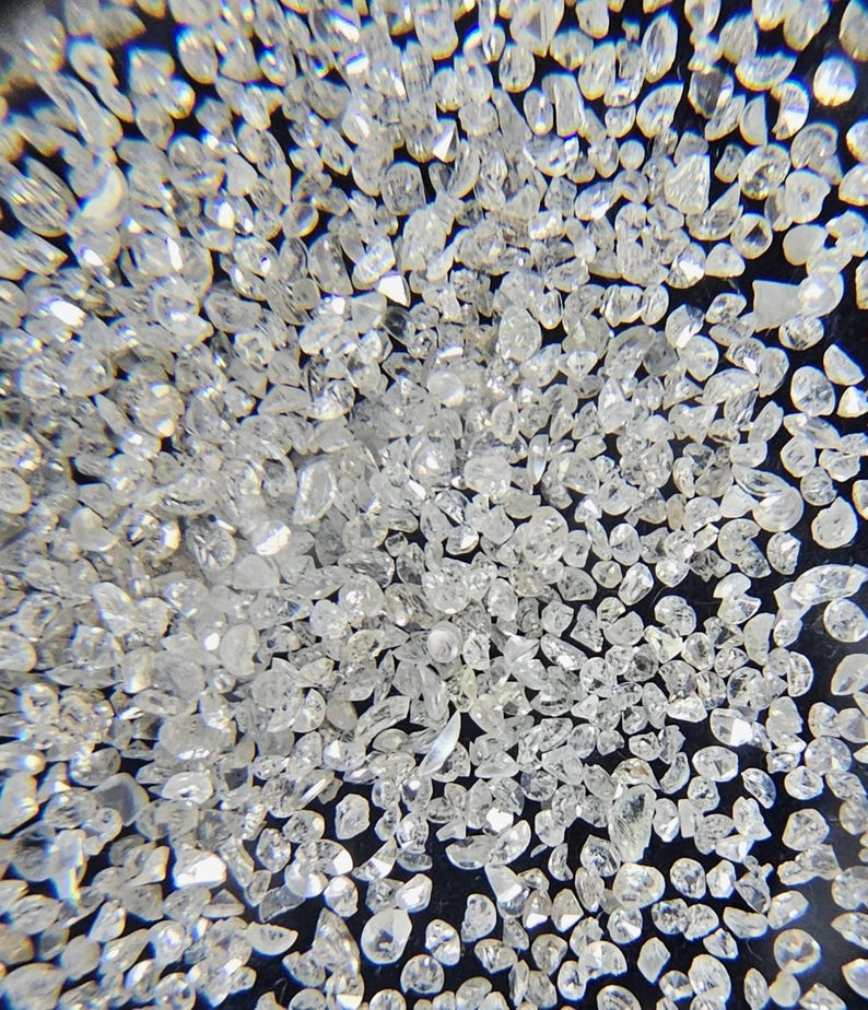 Puede incluir: Primer plano de una colecci&oacute;n de peque&ntilde;as gemas claras y facetadas. Las gemas est&aacute;n dispersas sobre una superficie oscura, reflejando la luz y creando un efecto brillante. Las formas var&iacute;an, lo que sugiere que son sin cortar o de corte basto.