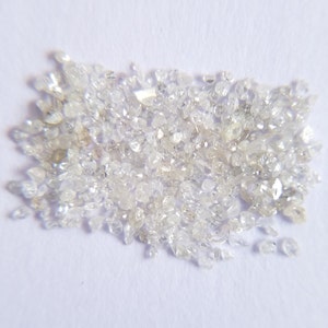 Puede incluir: Un conjunto de peque&ntilde;os diamantes claros de forma irregular, dispersos sobre una superficie blanca. Los diamantes var&iacute;an en tama&ntilde;o y reflejan la luz, creando un efecto brillante. La imagen muestra gemas en bruto sin cortar.