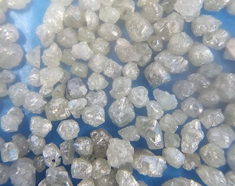 May include: A close-up view of a collection of small, rough, white diamonds. The diamonds are scattered on a blue surface.