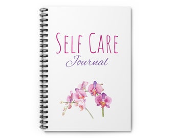 May include: A white spiral bound journal with the text "SELF CARE Journal" in pink lettering. The journal is decorated with a watercolor illustration of pink orchids.