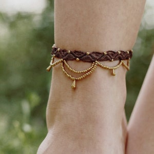 Op de afbeelding: Een bruine enkelband met gouden kralen en druppelvormige bedels.