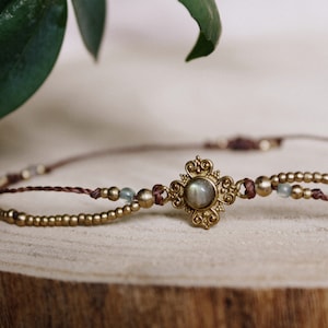 May include: A delicate gold necklace with a brown cord and small gold beads. A round, iridescent gemstone is set in a gold filigree pendant.
