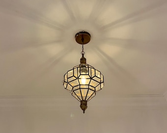 May include: A brass pendant light with a geometric design, hanging from the ceiling. The light has a faceted glass shade and a warm bulb. The fixture is suspended by a chain.