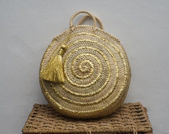 May include: A round straw bag with a gold metallic finish and a gold tassel. The bag has a woven design and a top handle.
