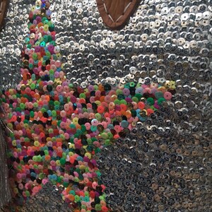 May include: Silver sequined handbag with a star-shaped design made of colorful sequins. The bag has a brown leather handle with white stitching. The sequins are in various colors, including pink, green, orange, and yellow.