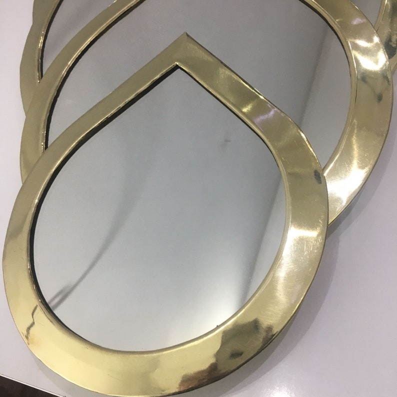 May include: A gold-toned, round, decorative mirror with a layered, overlapping design. The mirror has a smooth, polished surface.