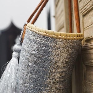 May include: A silver sequined tote bag with a brown leather handle and a silver tassel. The bag is hanging on a wooden wall.