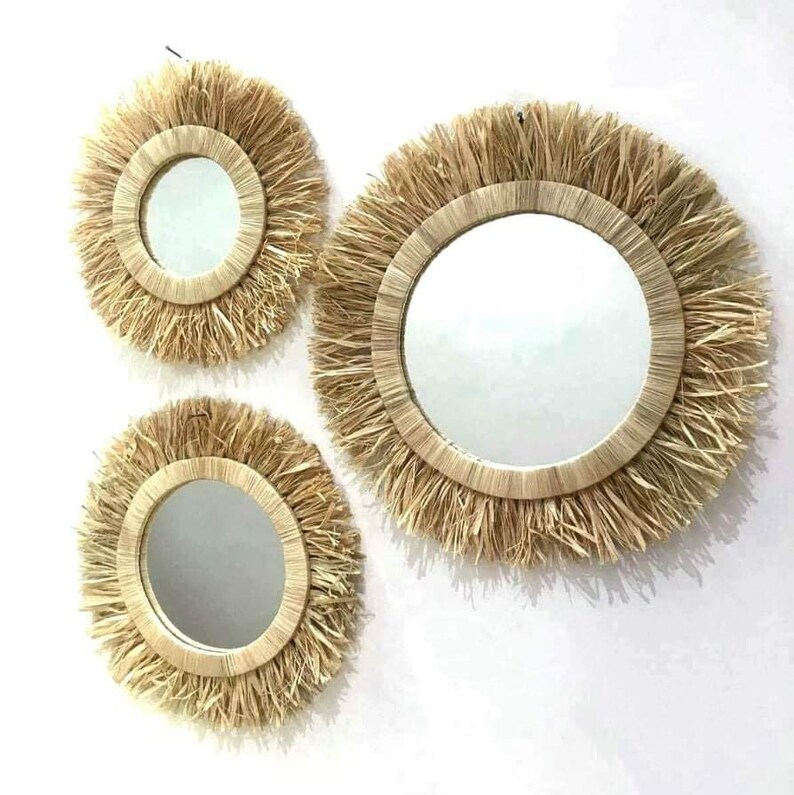 May include: Set of three round mirrors with natural woven straw frames. The mirrors are different sizes and have a natural, rustic look.