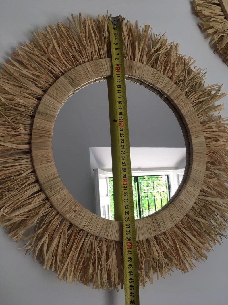 May include: A round mirror with a natural woven straw frame. The frame has a fringe of straw around the edge. The mirror is 40 inches in diameter.