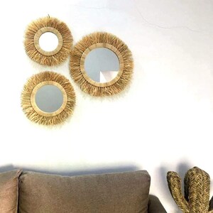 May include: Three round mirrors with natural woven frames, the largest mirror is in the center, the two smaller mirrors are on either side of the center mirror.