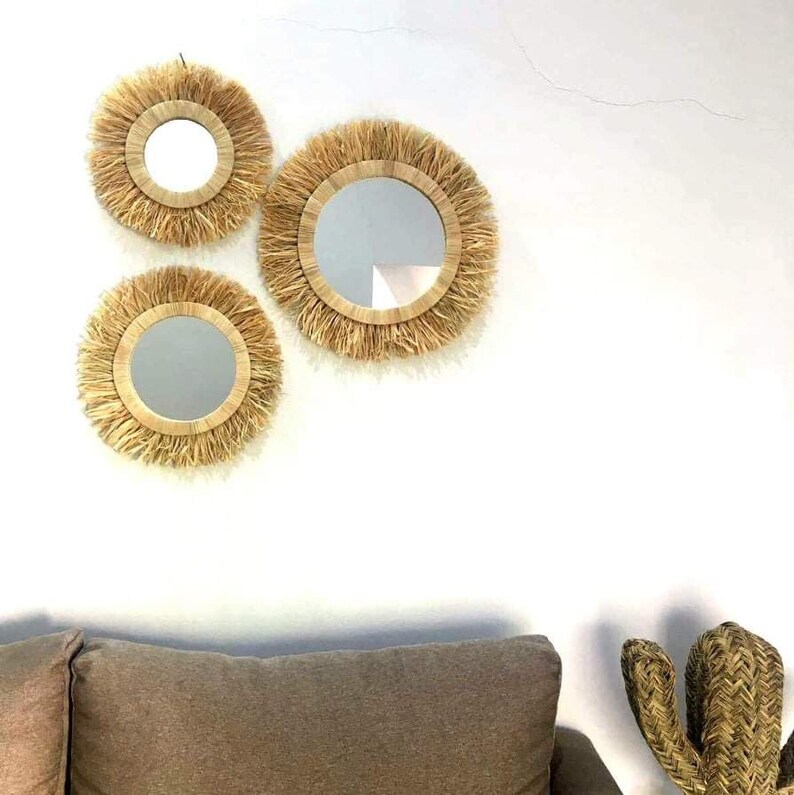 May include: Three round mirrors with natural woven frames, the largest mirror is in the center, the two smaller mirrors are on either side of the center mirror.