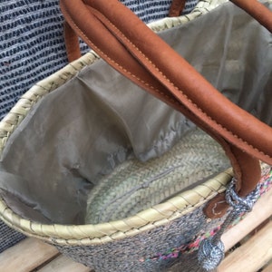 May include: Woven straw tote bag with brown leather handles and a gray interior lining. The bag features a decorative tassel and colorful accents. A stylish and practical accessory for carrying items.