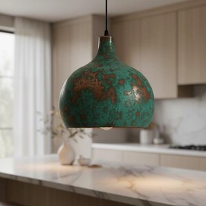 Puede incluir: L&aacute;mpara colgante con acabado moteado verde y marr&oacute;n. La l&aacute;mpara tiene forma redondeada de campana y cuelga de un cable negro. Cuelga sobre una isla de cocina, a&ntilde;adiendo un toque decorativo.