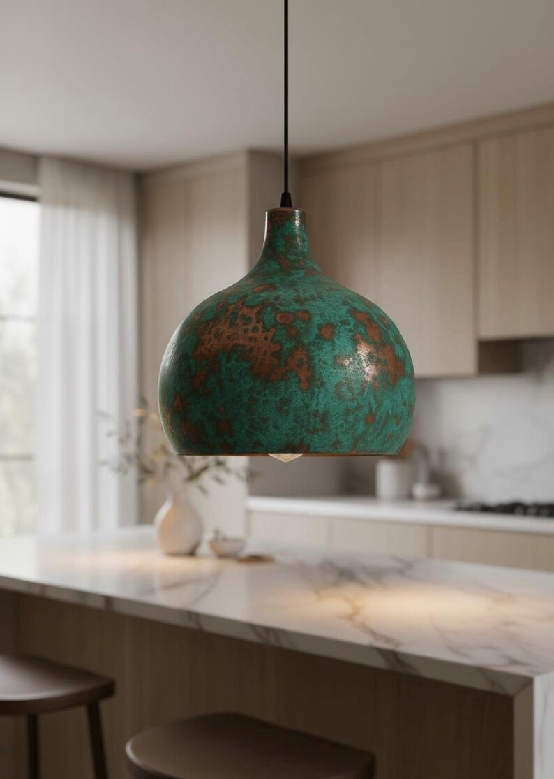Puede incluir: L&aacute;mpara colgante con acabado moteado verde y marr&oacute;n. La l&aacute;mpara tiene forma redondeada de campana y cuelga de un cable negro. Cuelga sobre una isla de cocina, a&ntilde;adiendo un toque decorativo.