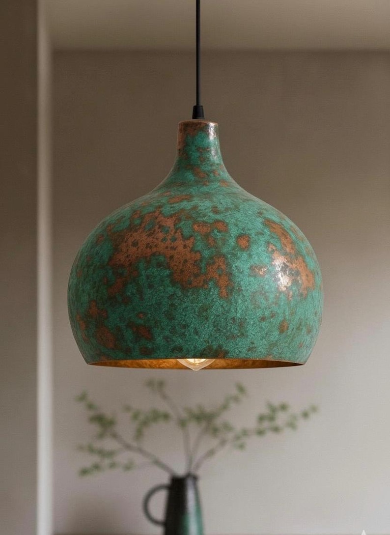 Puede incluir: L&aacute;mpara colgante con acabado verde y cobre. La l&aacute;mpara tiene una pantalla redondeada en forma de campana con una superficie texturizada. El interior de la pantalla es de color dorado y se ve una sola bombilla.