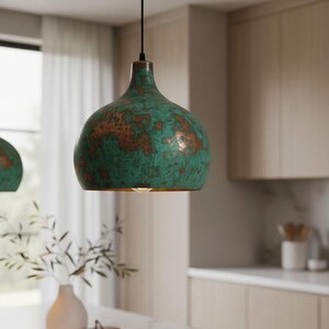 Puede incluir: Una l&aacute;mpara colgante verde y cobriza de forma redondeada cuelga de un cable negro. La luz tiene un acabado envejecido y est&aacute; suspendida sobre una encimera de cocina. El accesorio es un elemento decorativo.