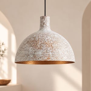 May include: A dome-shaped pendant light fixture featuring a white exterior with a textured, distressed finish that reveals a metallic copper base layer. The interior of the shade is finished in a smooth, reflective copper tone, suspended by a black cord.