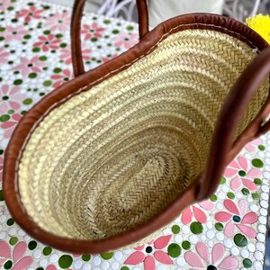 May include: A brown leather-trimmed straw tote bag with a woven design. The bag is empty and the inside is visible.