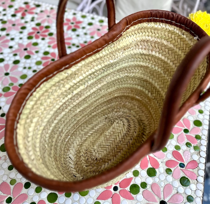 May include: A brown leather-trimmed straw tote bag with a woven design. The bag is empty and the inside is visible.
