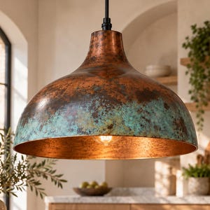 May include: A dome-shaped pendant light fixture with a weathered copper finish featuring prominent teal and green oxidation patches. The interior of the metal shade is a smooth, polished copper tone, and a single light bulb is visible inside.
