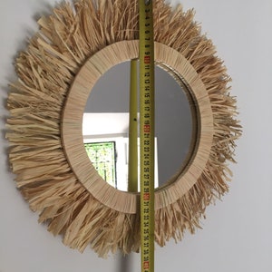 May include: A round mirror with a natural woven frame and a fringe of natural fibers. The mirror is 30 inches in diameter.