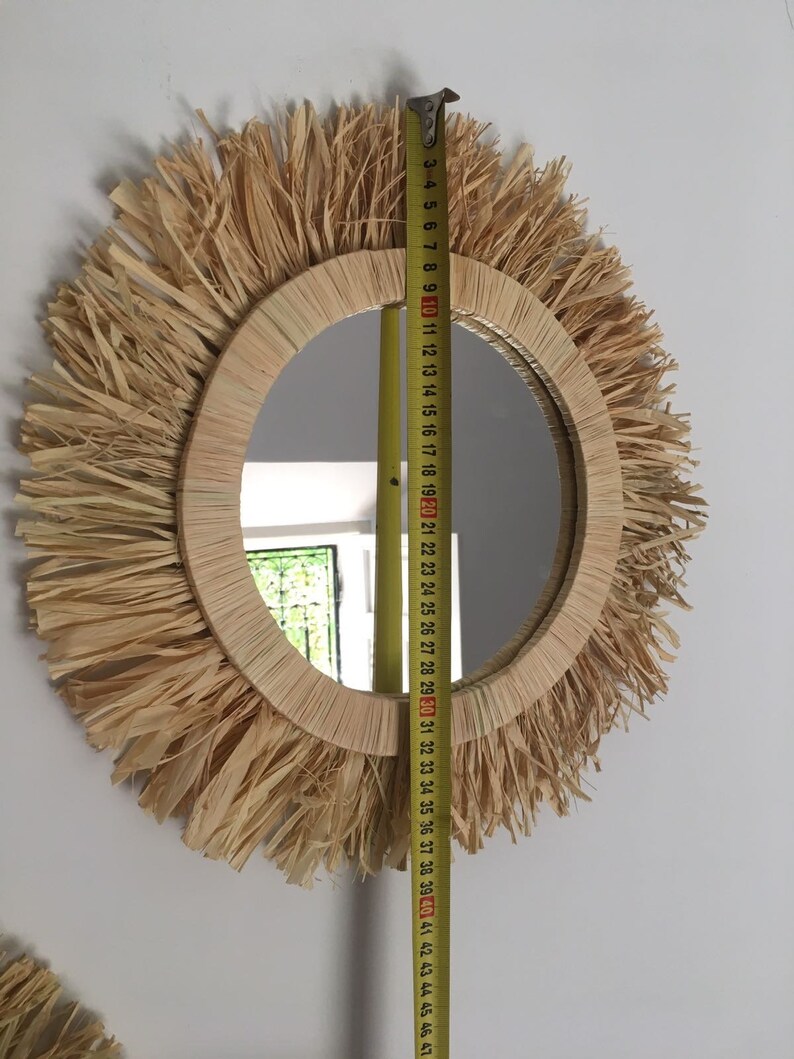 May include: A round mirror with a natural woven frame and a fringe of natural fibers. The mirror is 30 inches in diameter.