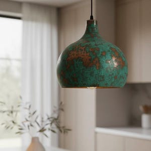 Puede incluir: L&aacute;mpara colgante con acabado verde y cobre. La l&aacute;mpara tiene una pantalla redondeada en forma de campana con una superficie texturizada. La luz cuelga de un cable negro, en un entorno de cocina.