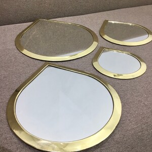 May include: Set of four gold-toned teardrop-shaped mirrors of varying sizes. The mirrors have a smooth, reflective surface and a thick, rounded frame.
