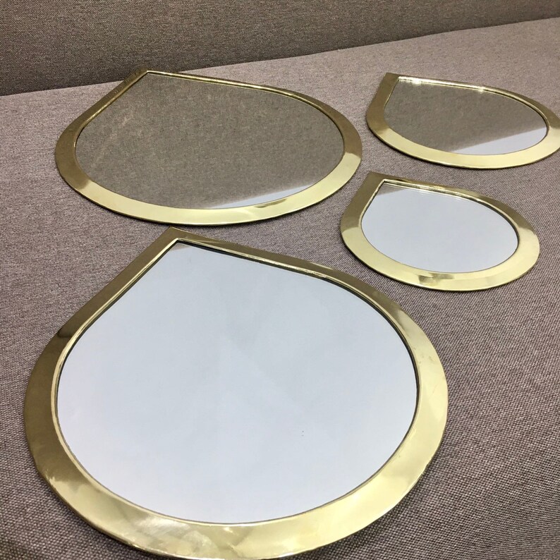 May include: Set of four gold-toned teardrop-shaped mirrors of varying sizes. The mirrors have a smooth, reflective surface and a thick, rounded frame.