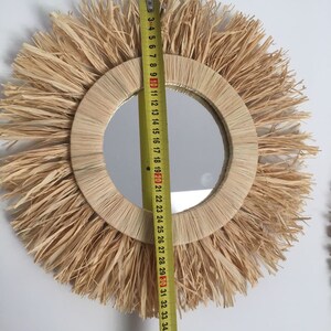 May include: A round mirror with a natural woven straw frame and a fringe border. The mirror is 30 inches in diameter.
