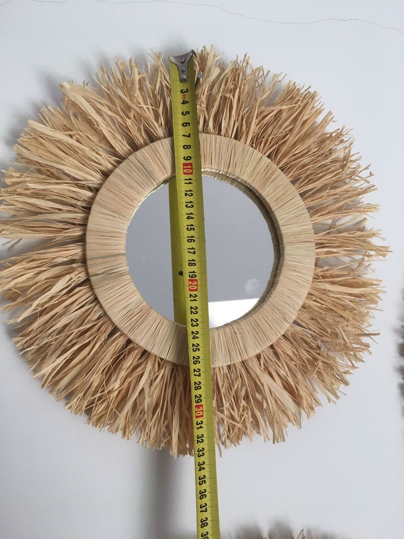 May include: A round mirror with a natural woven straw frame and a fringe border. The mirror is 30 inches in diameter.